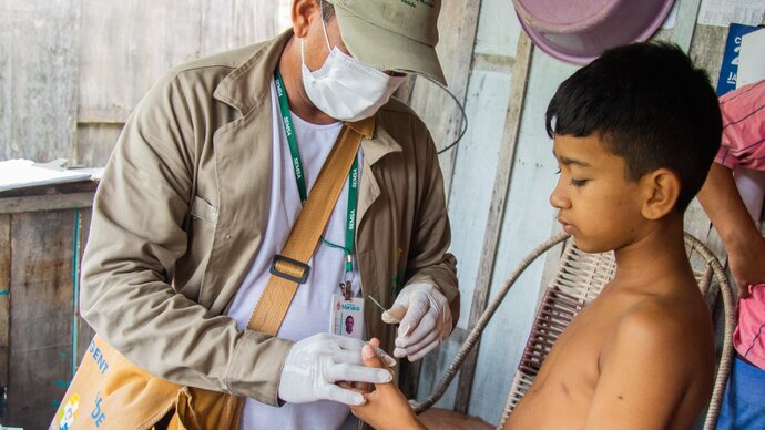 Health worker taking finger prick blood test from child in Brazil