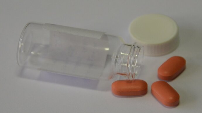 three pills of tafenoquine medicine next to glass pill jar