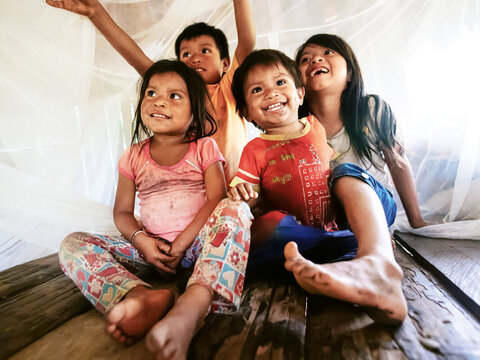 children sitting under a mosquito bed net.