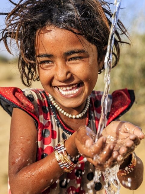 Una niña sonríe mientras le cae agua de un grifo en las manos